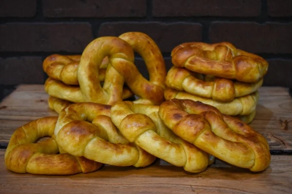 Twelve soft pretzel twists from Campbell Creek Pretzels piled on a wooden table with a brick wall in the background.
