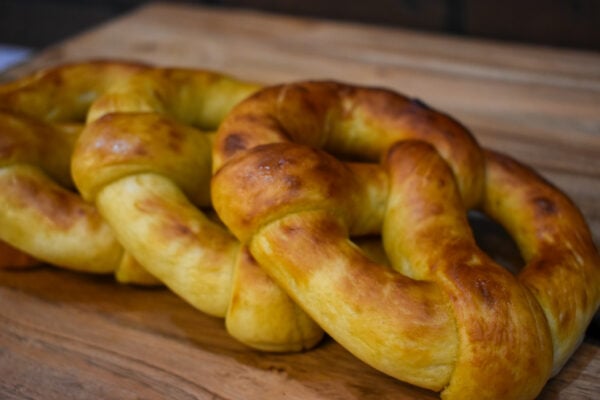 Four soft pretzel twists from Campbell Creek Pretzels piled on a wooden table with a brick wall in the background.