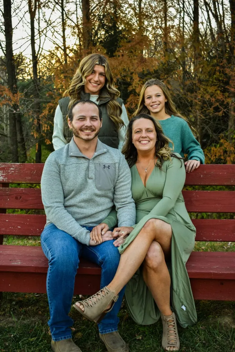 Amber Warner and her husband sit on a red bench with their two daughters standing behind them.
