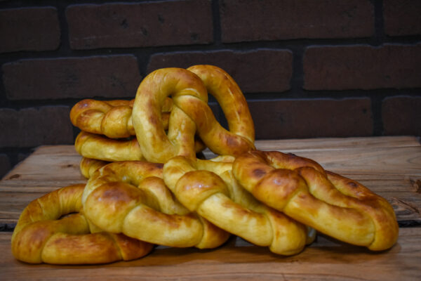Eight soft pretzel twists from Campbell Creek Pretzels piled on a wooden table with a brick wall in the background.